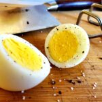 a sliced hard boiled egg seasoned with cracked black pepper and sea salt on a cutting board