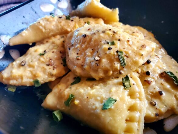 A picture of homemade mezzelune egg pasta drizzled in a homemade sauce.