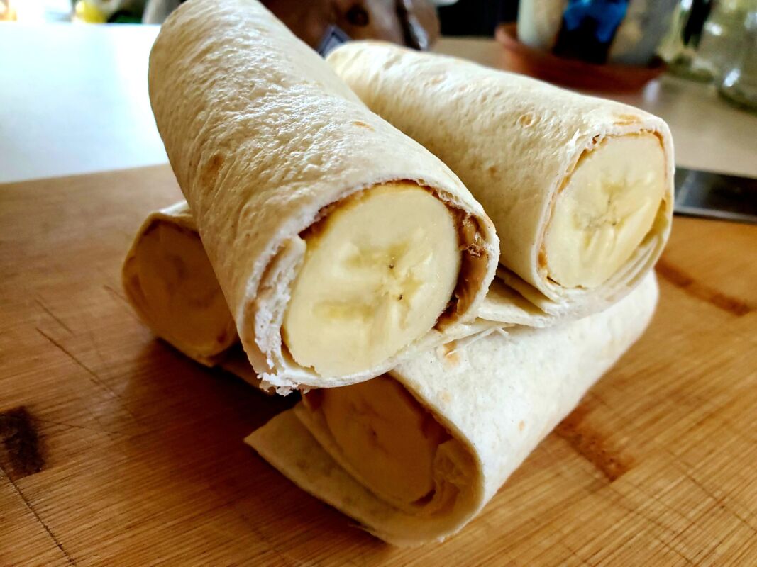 peanut butter and bananas rolled inside of a tortilla, cut in half and stacked up on a cutting board