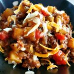 A picture of ground beef and potatoes cowboy skillet topped with shredded cheese in a bowl.