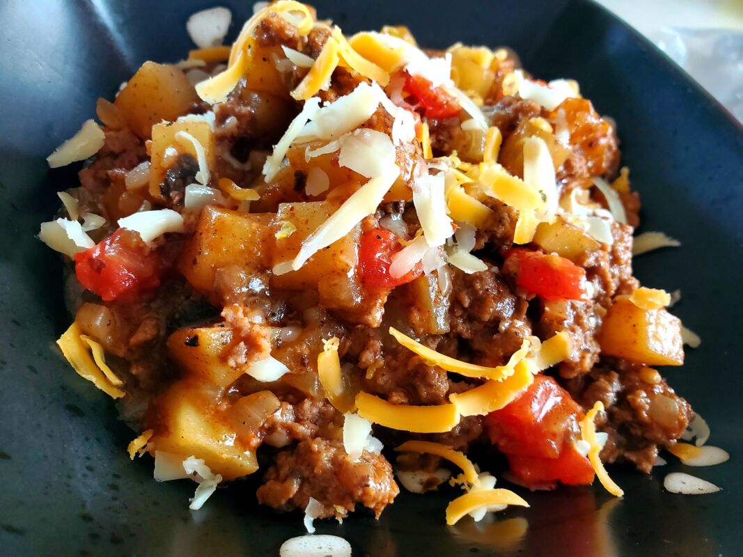 A picture of ground beef and potatoes cowboy skillet topped with shredded cheese in a bowl.