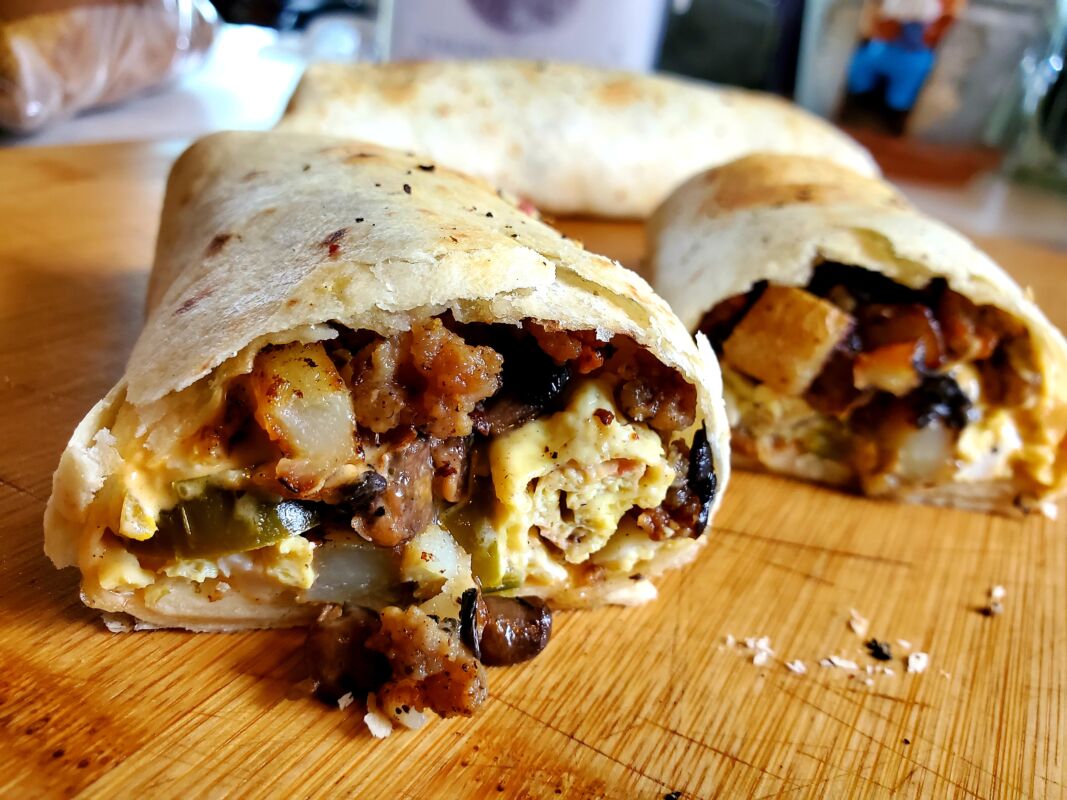 A picture of a breakfast burrito cut in half, displaying the contents inside.