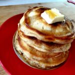 A picture of a stack of fluffy homemade pancakes with syrup drizzled over the top.