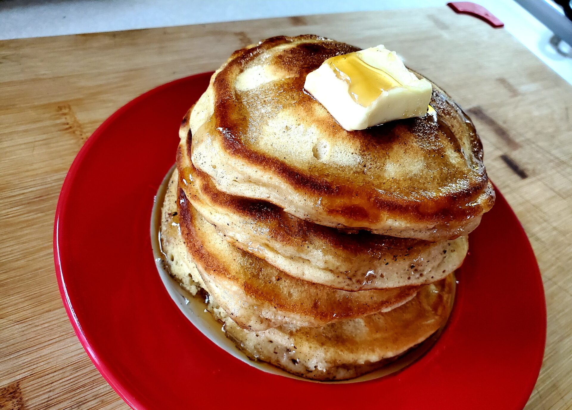 A picture of a stack of fluffy homemade pancakes with syrup drizzled over the top.